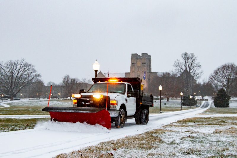 A truck with a snowplow clears snow that has accumulated on a walkway on the Drillfield.