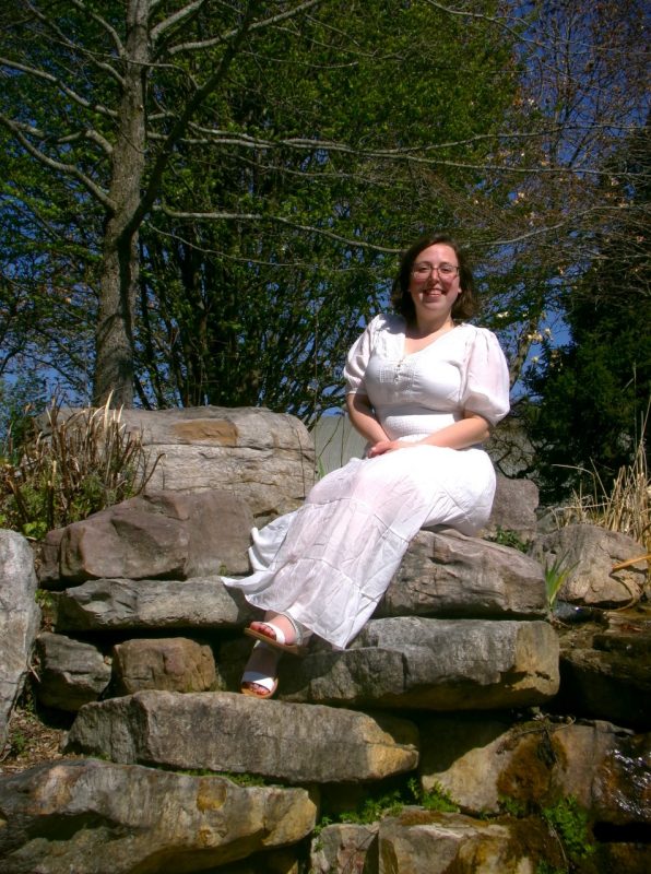 Student in white dress sits on rocks.