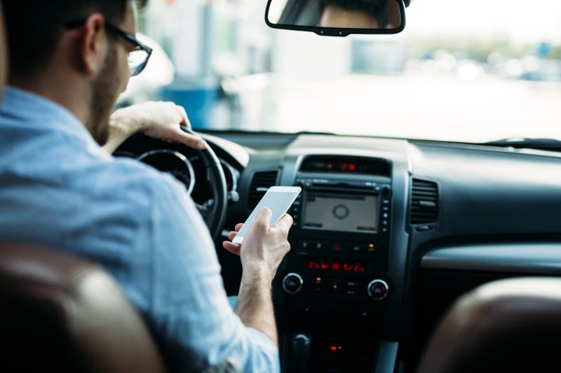 Man looks at phone while behind the wheel of a car.