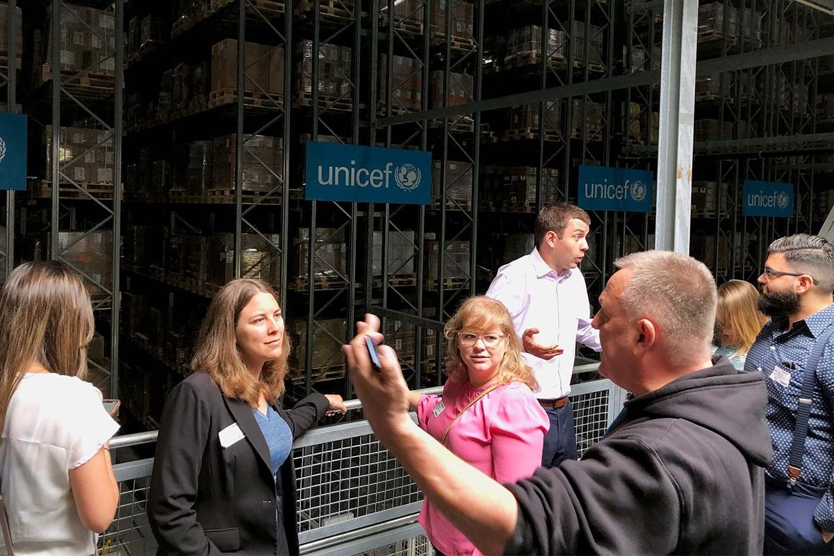 The group tours UNICEF’s supply division in Copenhagen, Denmark, led by warehouse supervisor John Roger Nielsen. Sabrina Kramer and Michele Hansen listen as Nielsen explains how UNICEF works with government and company partners to strengthen supply chains that deliver essential goods supporting child survival and development around the world. (Photo Credit: Barbara Hoopes)