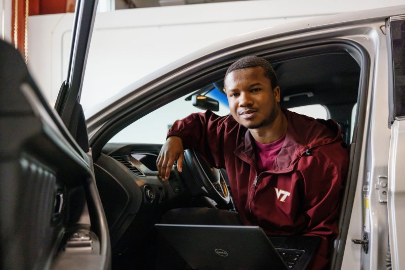 Student wearing a VT shirt looks up from a computer from the front seat of a parked car