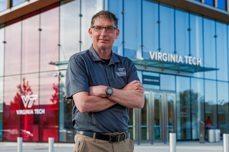 A man standing with his arms crossed in front of a glass building