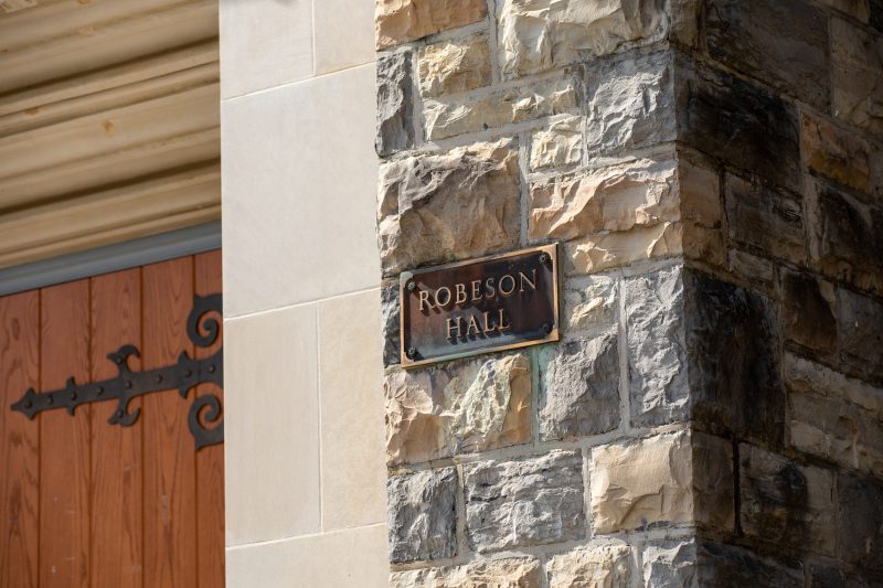 Bronze plaque with the words Robeson Hall on it. The plaque is on a grey Hokie Stone wall next to the building's entryway.