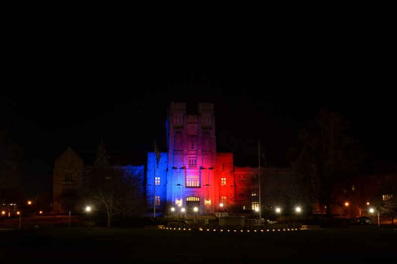 Burruss Hall illuminated red and blue at nighttime, with one side of the building being red and the other blue